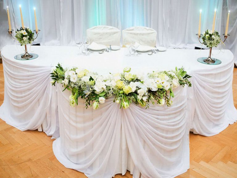Vestuvių stalas su baltu dekoravimo audiniu ir žvakidėmis