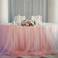 Šviesus tiulio sijonas aplink vestuvių stalą