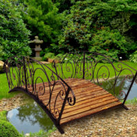 Wooden bridge with forged railing over the garden pond