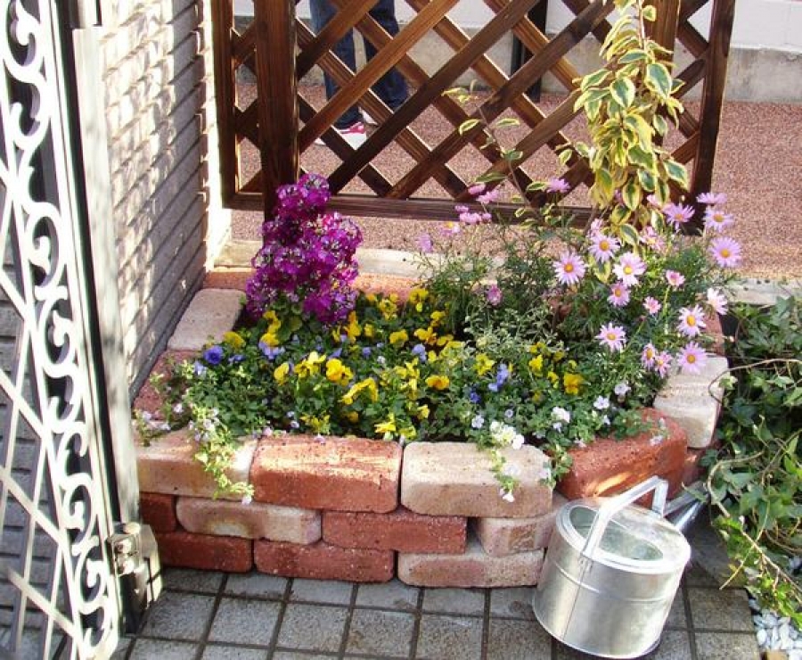 Parterre de fleurs en brique devant la porte et un arrosoir pour l'arrosage