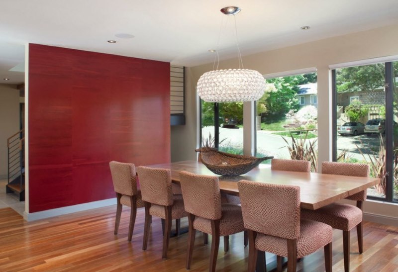 A good combination of a red wall with dark beige chairs in the dining area