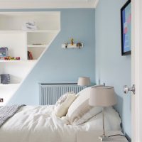 Mėlynos sienos miegamajame su balta lova.