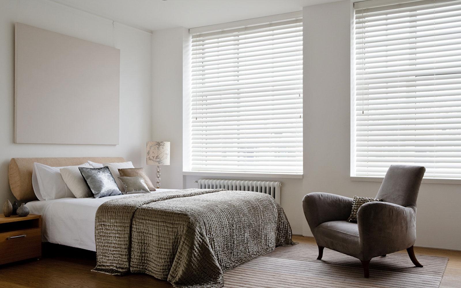 White horizontal blinds in a bedroom with a gray bedspread