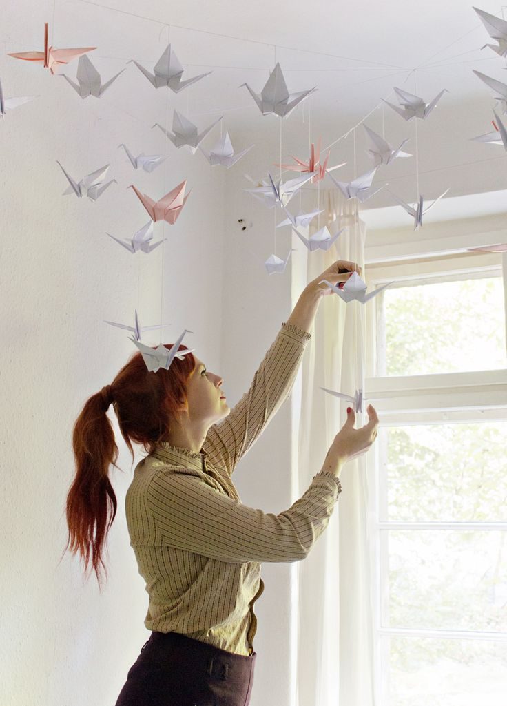 Mom hangs paper figures of cranes on the ceiling of the room.