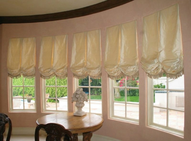 Beige Austrian curtains on the narrow windows of a bay window in a private house