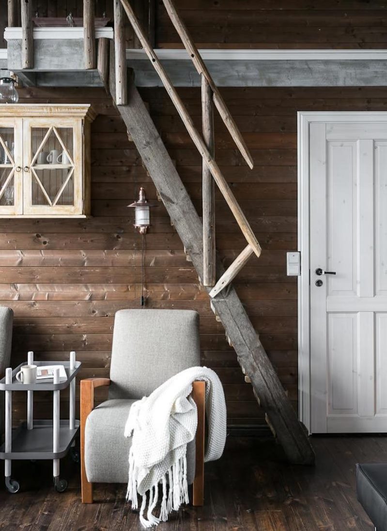 Gray armchair under a steep staircase to the second floor of a wooden house