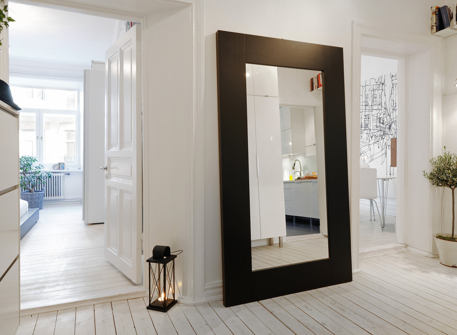 Specchio in un'ampia cornice nera sul pavimento di un corridoio bianco